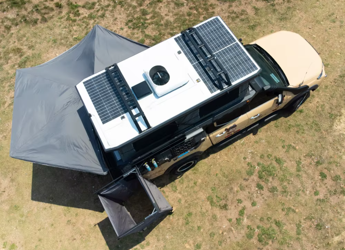 Aerial view of Iron Den Overland slide in camper with 270 degree awning deployed, shower tent set up, roof mounted solar panels, and pop up tent fully opened
